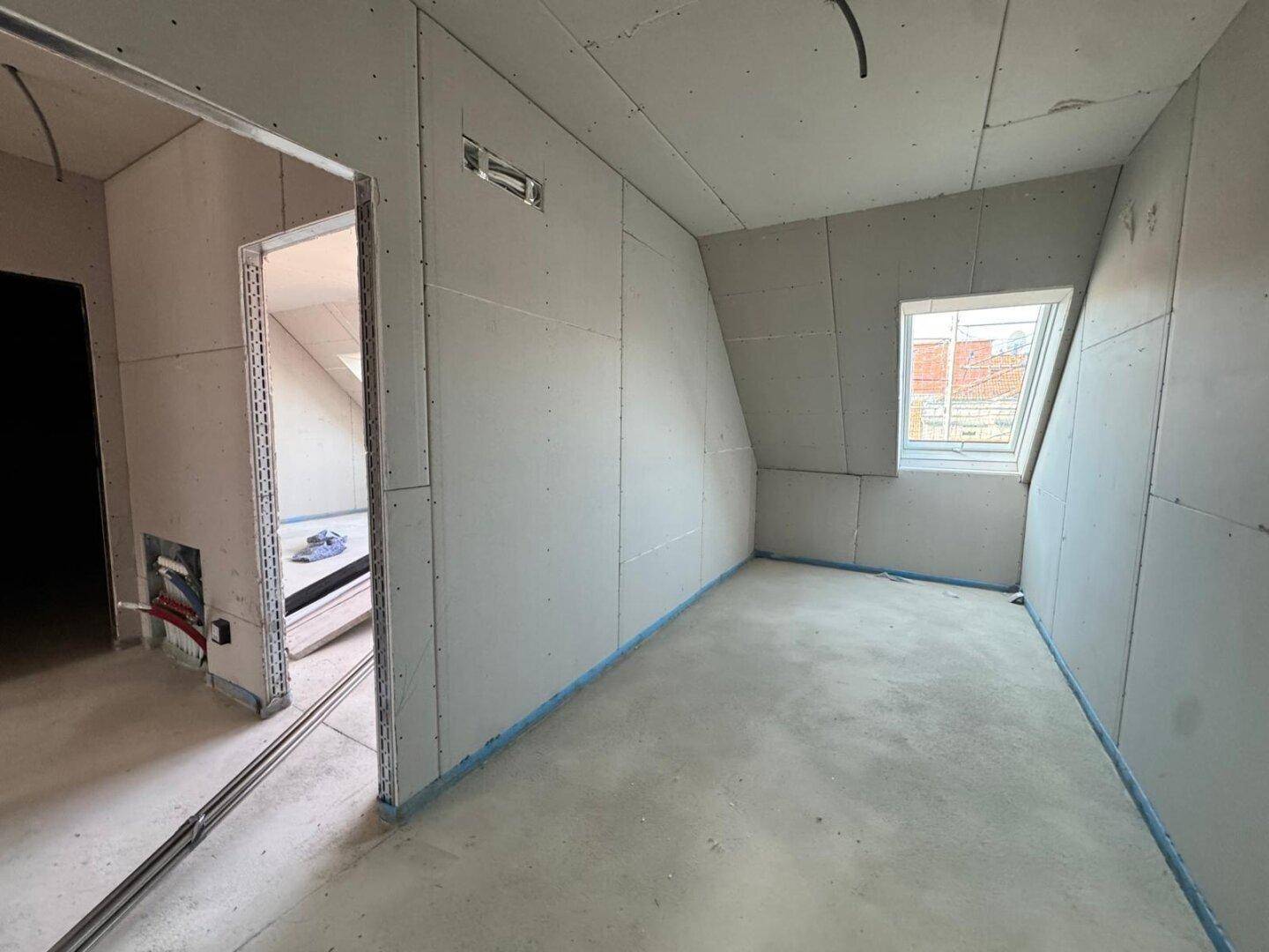 Rohbau eines kleineren Raumes mit Trockenbauwänden und einem Dachfenster, bereit für den Ausbau.
