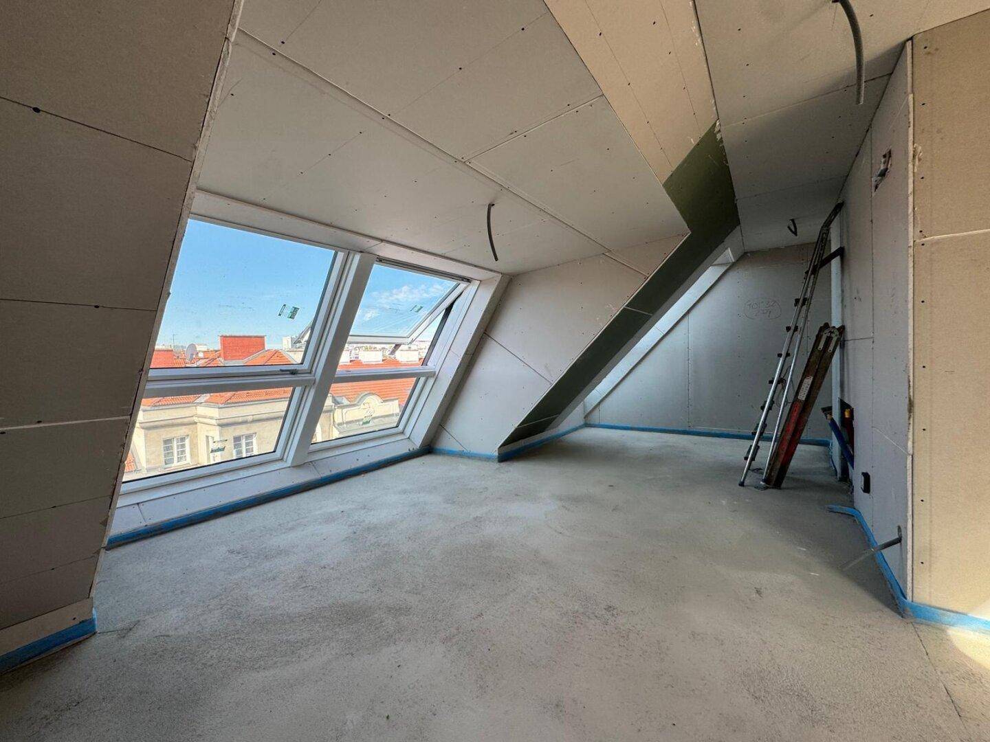 Raum im Rohbau mit Trockenbauwänden, Betonboden und großen Dachfenstern, bereit für den Ausbau.