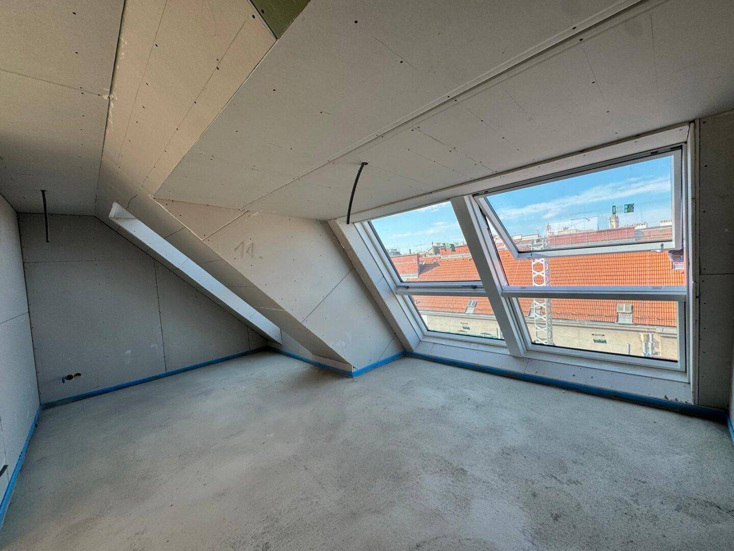 Raum im Rohbau mit Trockenbauwänden, Betonboden und Dachfenstern, die viel Licht spenden.