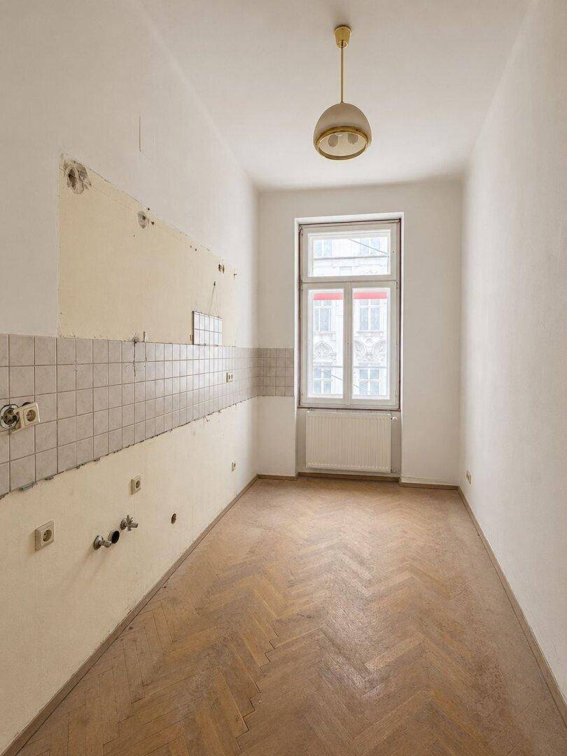 Leere Küche mit Fliesenrückwand und Fischgrätparkett, bereit für neue Einbauten.