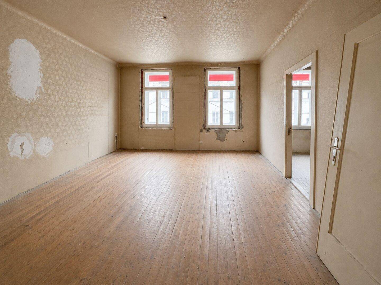 Unrenoviertes Zimmer mit abgenutztem Holzboden und beschädigten Wänden, wartet auf Modernisierung.