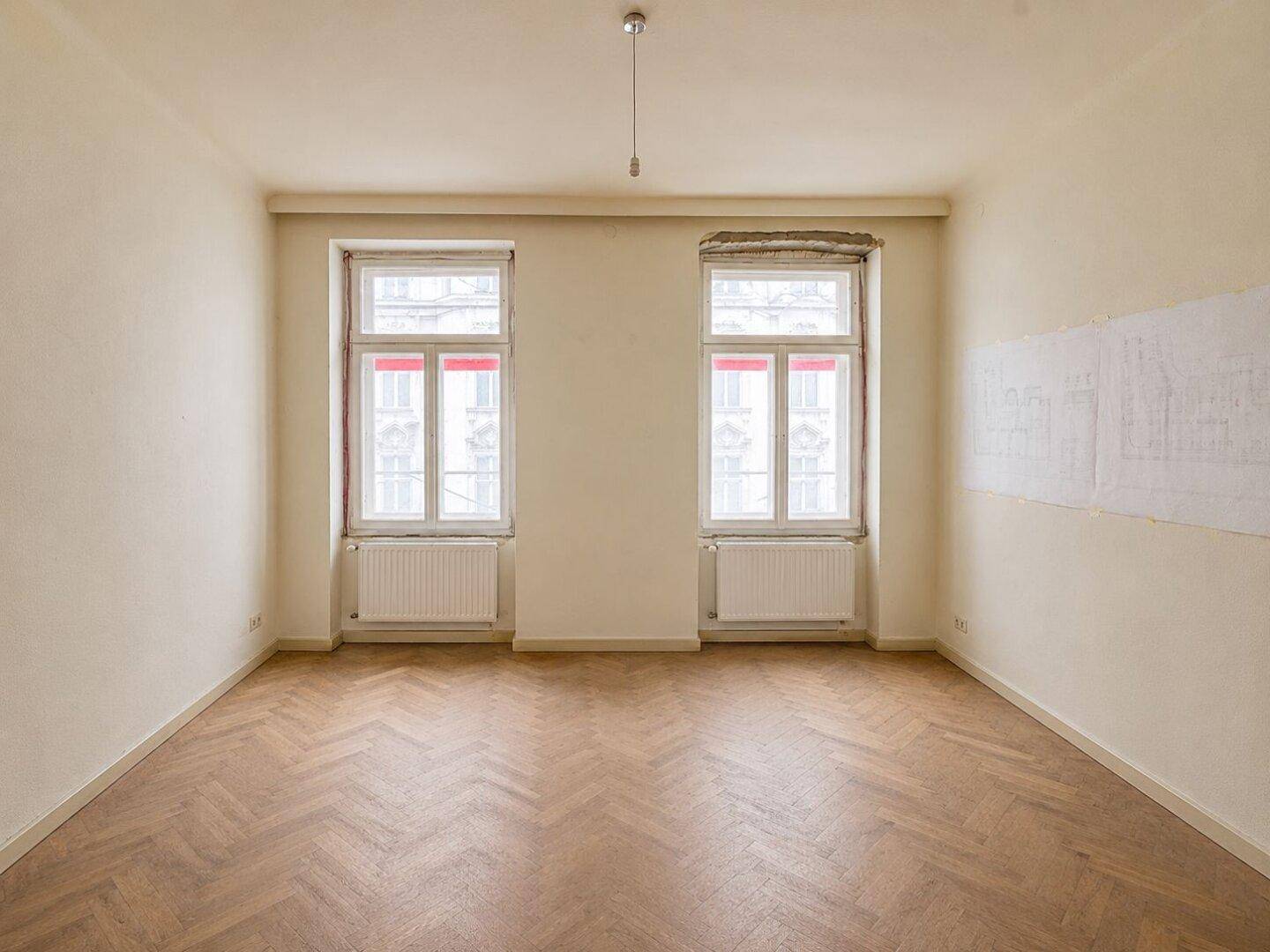 Helles Zimmer mit Fischgrätparkett und zwei Fenstern, ideal für Schlaf- oder Wohnbereich.