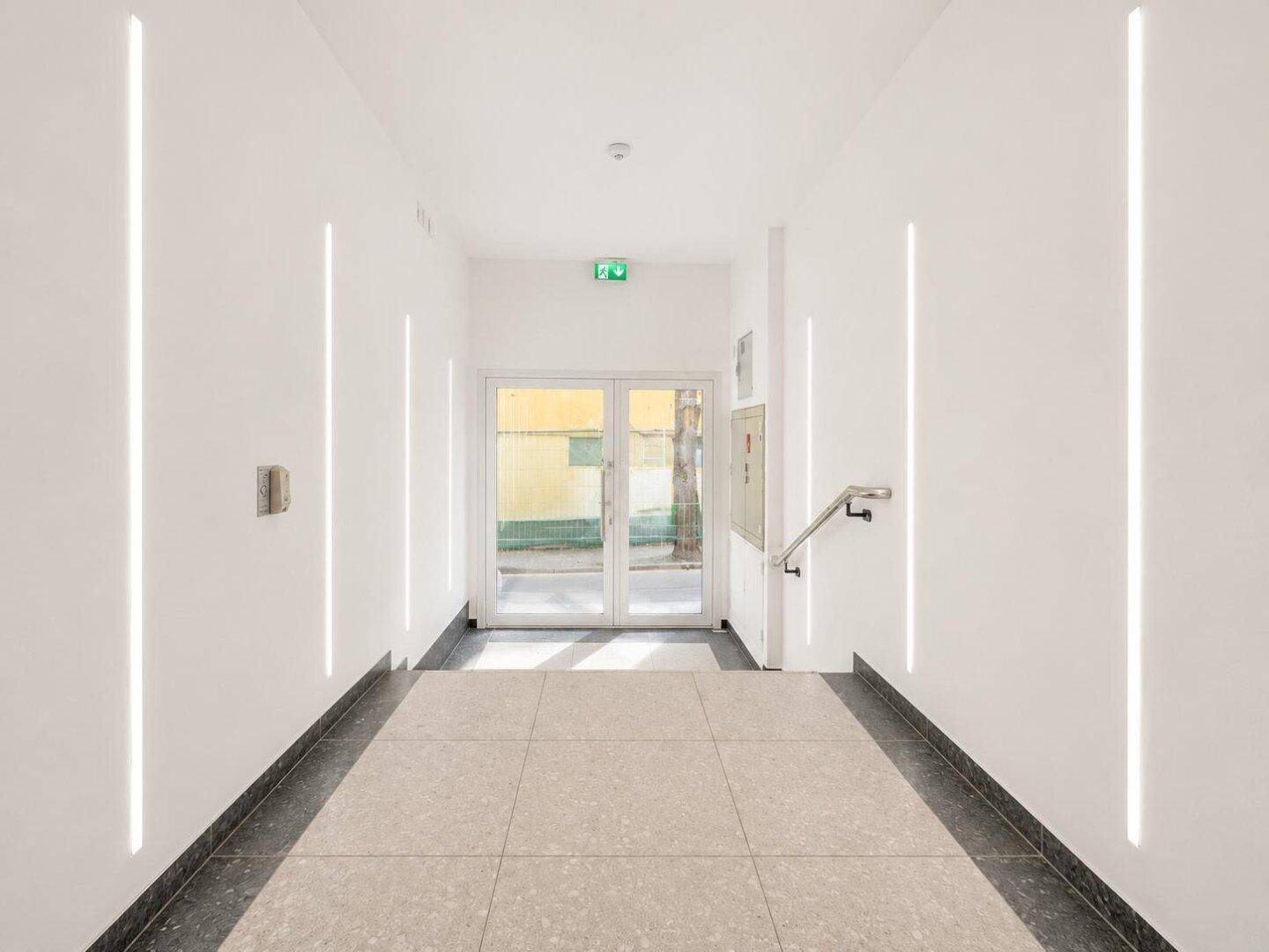 Moderner und heller Flur mit Fliesenboden und vertikalen Lichtelementen.