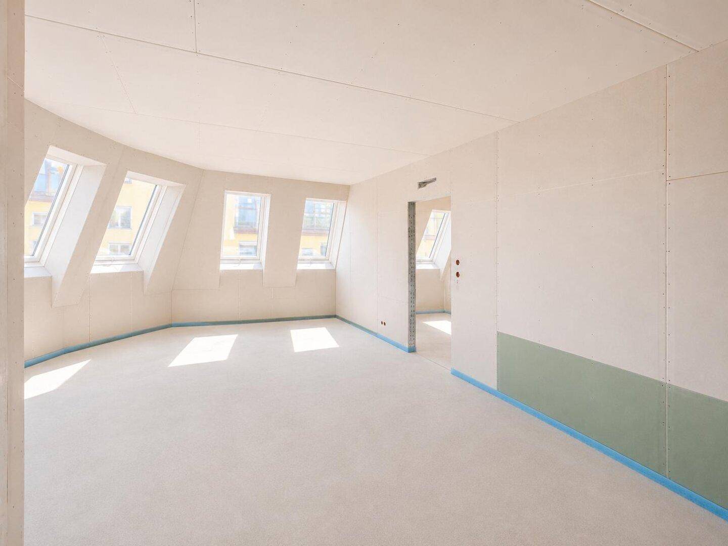Geräumiger, unfertiger Raum mit schrägen Wänden und Dachfenstern, bereit für den Ausbau.