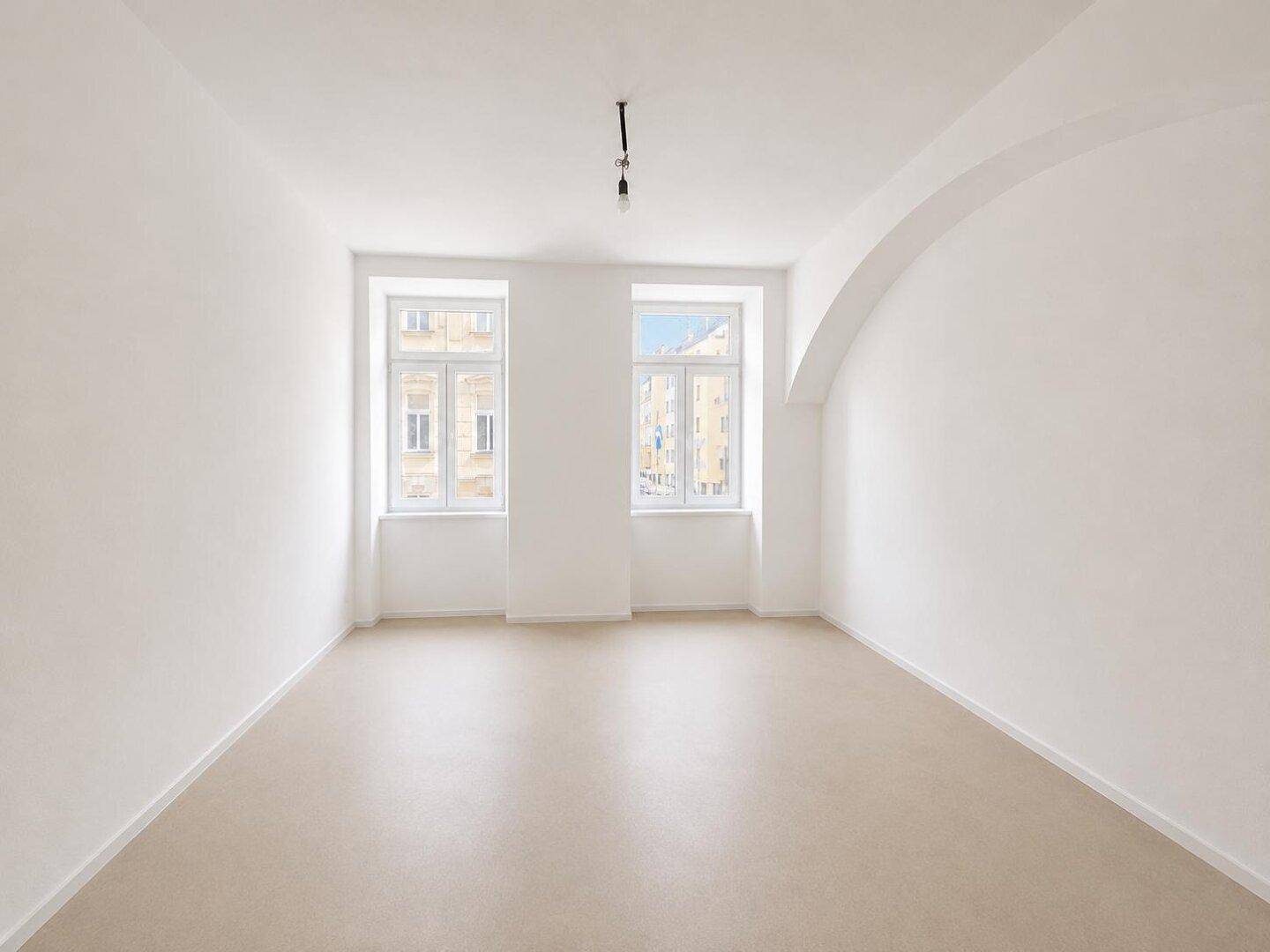 Heller, leerer Raum mit einer architektonischen Rundung an der Decke und zwei Fenstern.