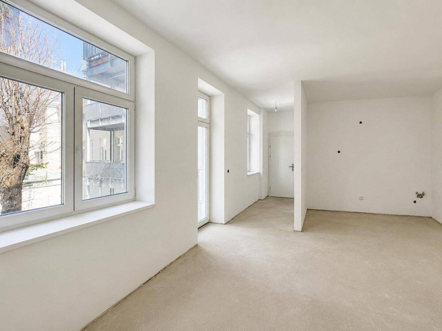Heller, unmöblierter Raum mit großen Fenstern und Zugang zu einem französischen Balkon.