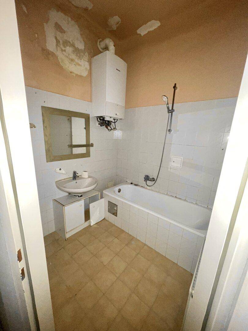 Badezimmer mit Badewanne, Waschbecken und Wandfliesen, das eine Modernisierung benötigt.