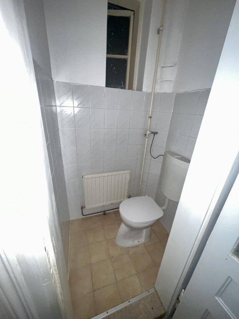 Separates WC mit Toilette, Fliesen und einem kleinen Fenster für natürliche Belüftung.