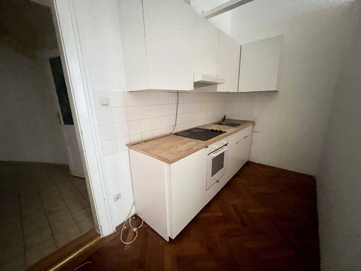 Kleine Einbauküche mit weißen Schränken, Holzarbeitsplatte und integriertem Kochfeld und Ofen.