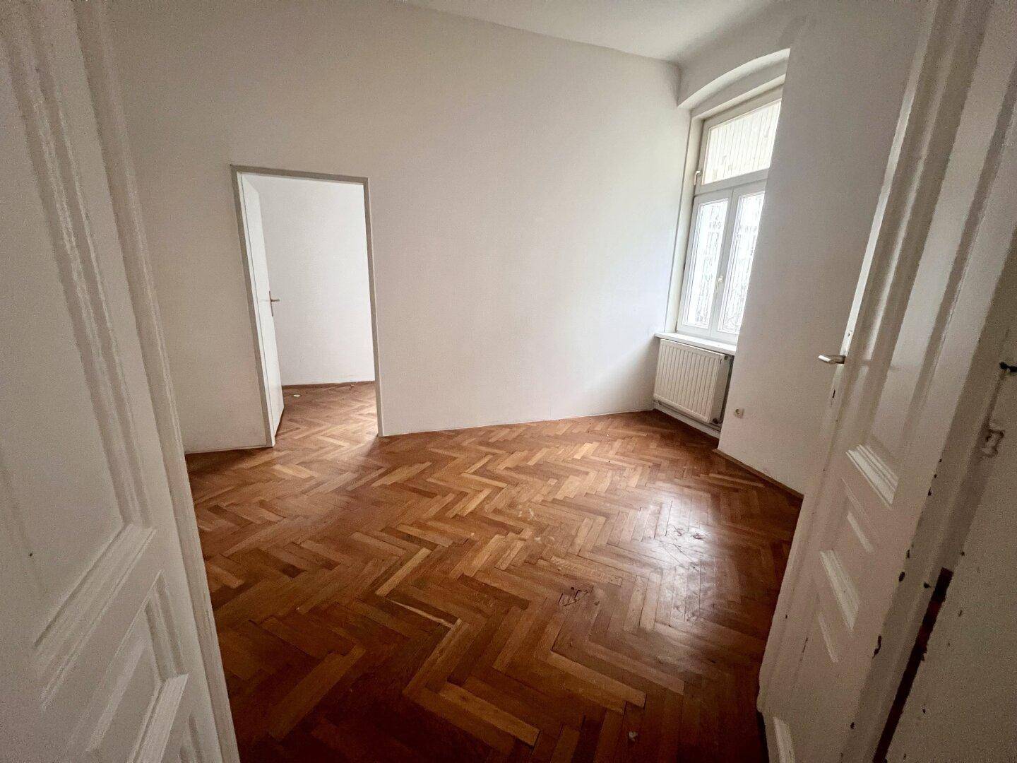 Leeres Zimmer mit Fischgrätparkett und einem Fenster, ideal als Schlaf- oder Arbeitszimmer.