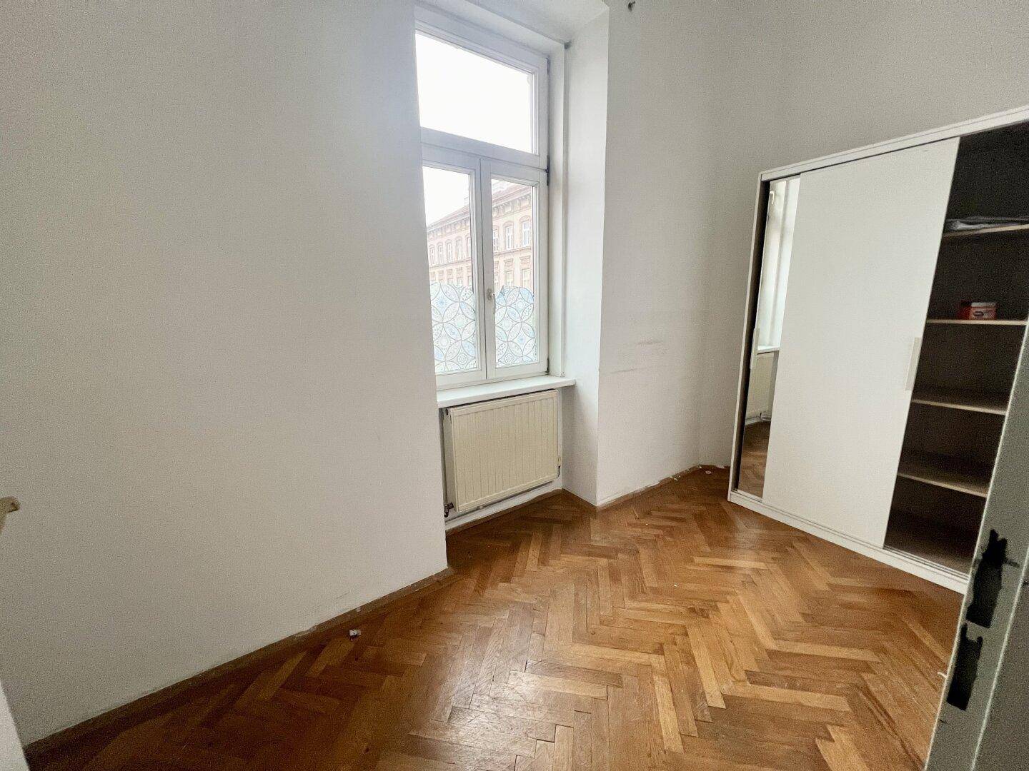 Zimmer mit Fischgrätparkett und einem großen Einbauschrank mit Spiegeltüren.