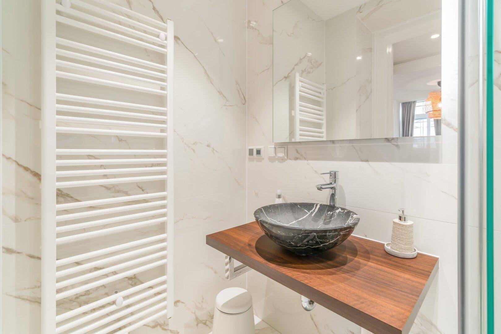 Modernes Badezimmer mit Marmorfliesen, stilvollem Waschbecken und beheiztem Handtuchhalter.