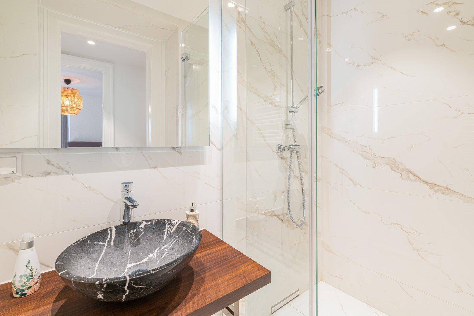 Elegantes Badezimmer mit Marmorfliesen, modernem Waschbecken und einer Duschkabine aus Glas.