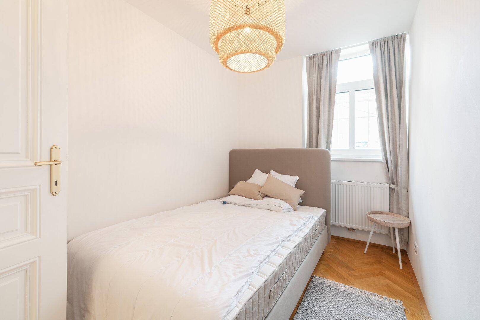 Kleines Schlafzimmer mit Einzelbett, hellem Holzboden und einem Fenster mit Vorhängen.