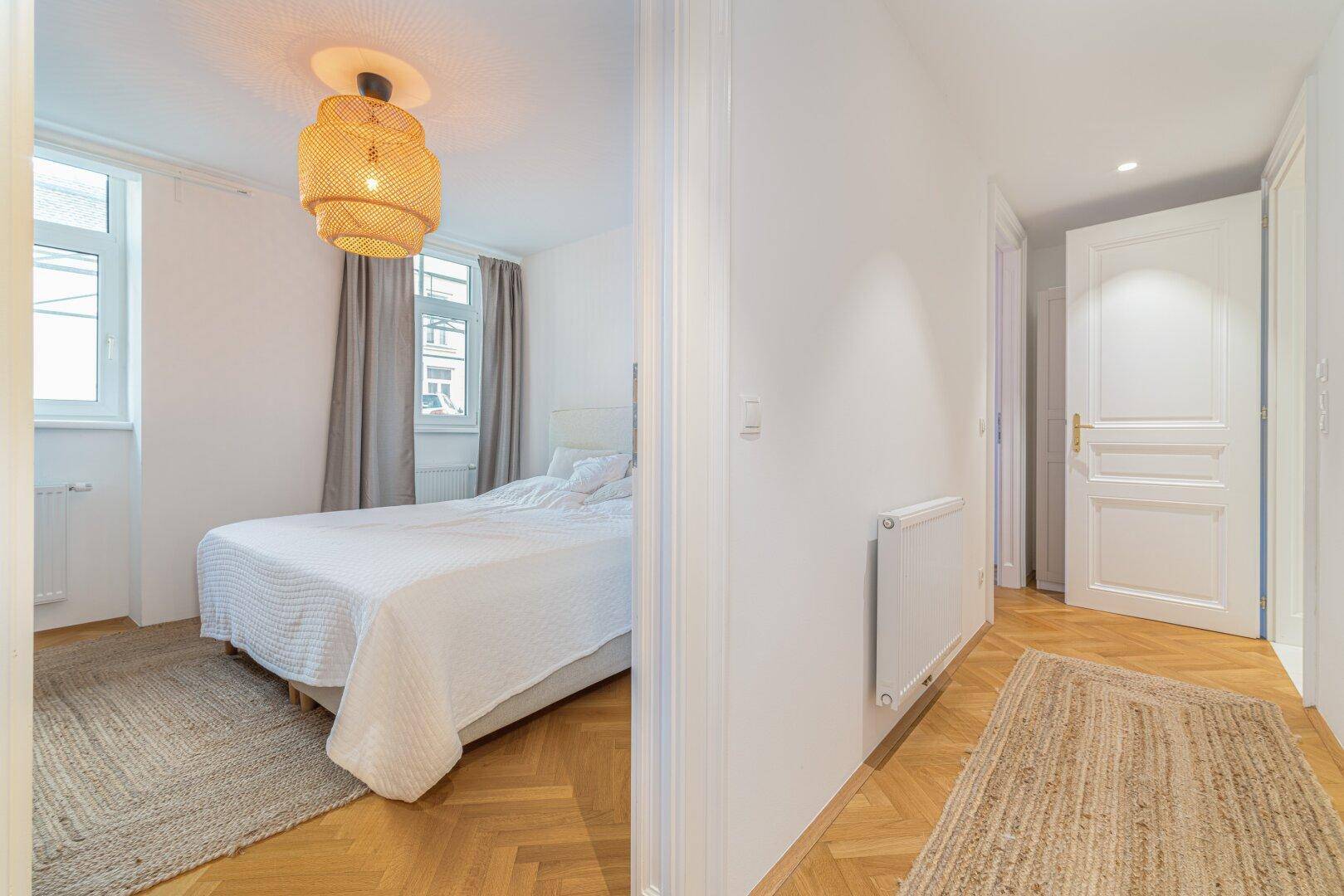 Heller Flur mit Fischgrätparkett, der in ein gemütliches Schlafzimmer führt.