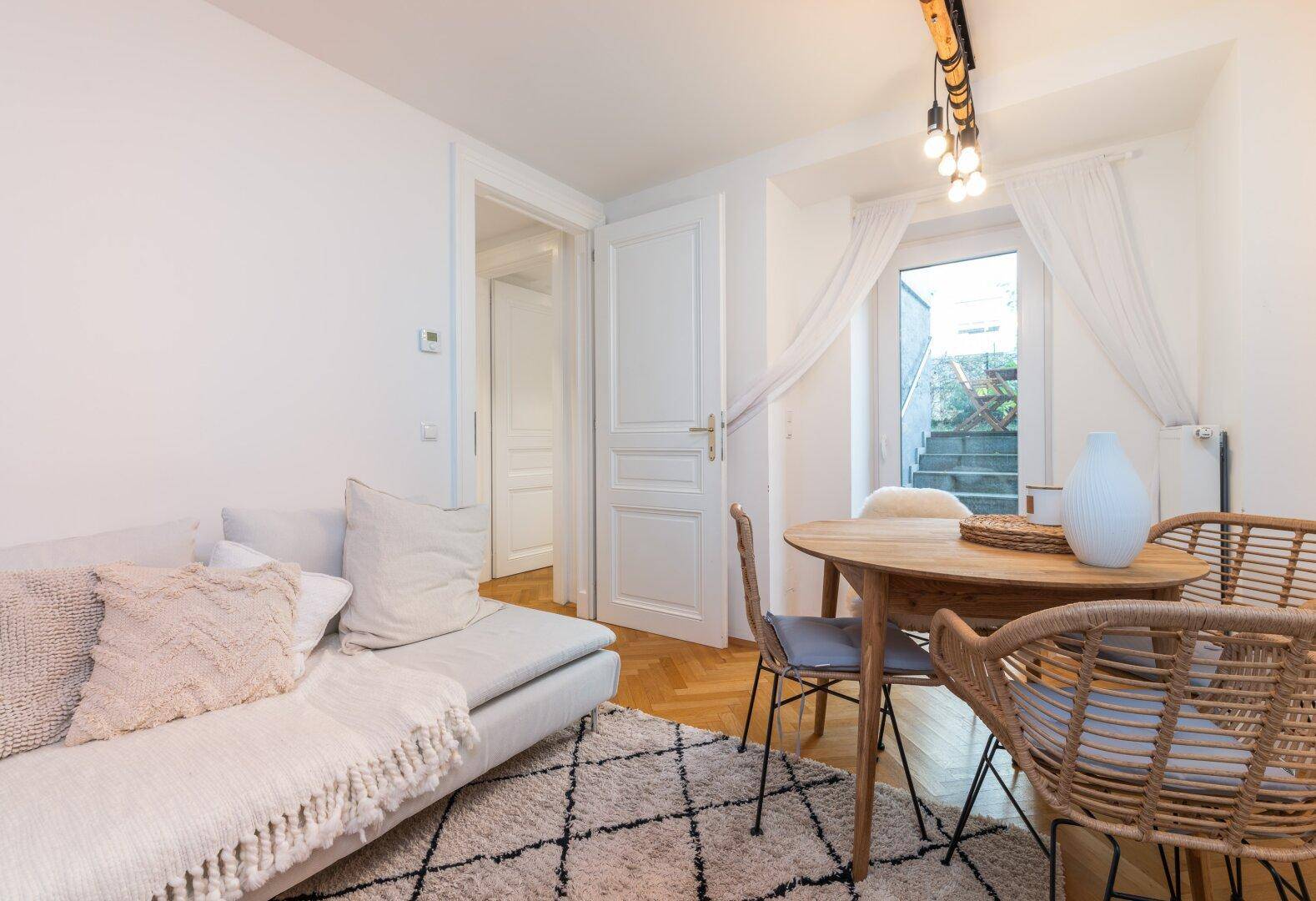 Heller Wohnbereich mit Sofa, Esstisch und Zugang zu einem Außenbereich mit Treppe.