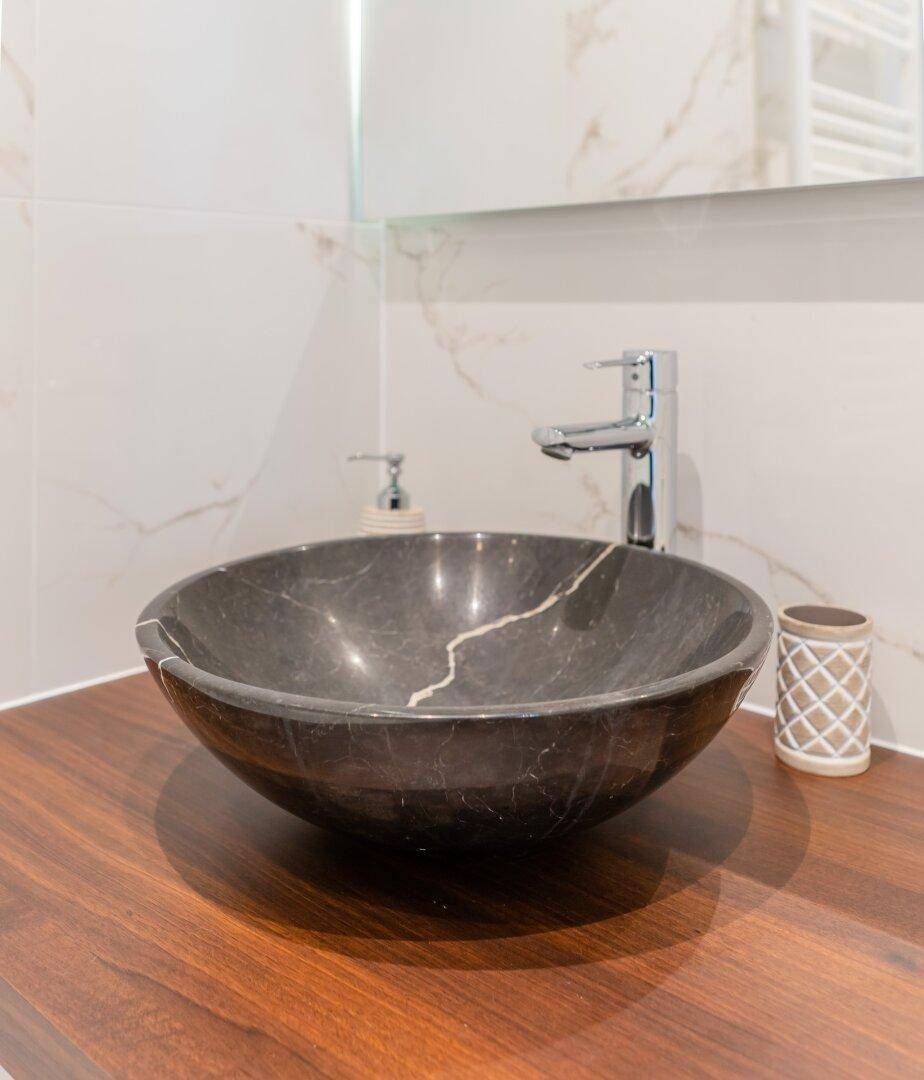 Detailaufnahme des modernen Waschbeckens aus dunklem Marmor auf einer Holzplatte im Badezimmer.