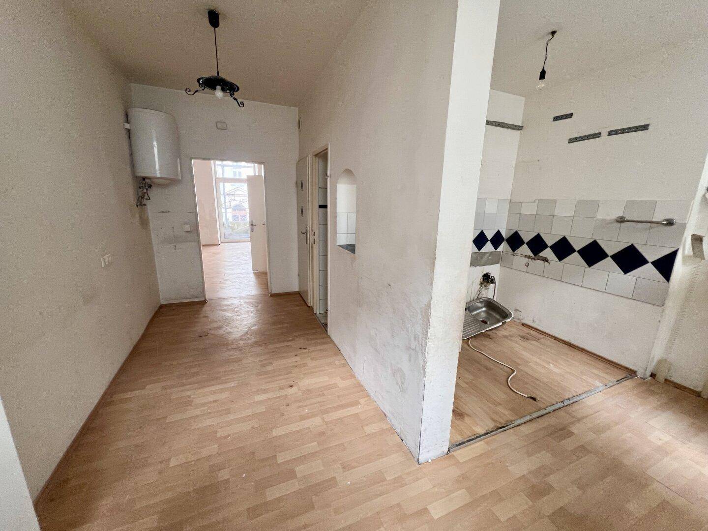 Eingangsbereich führt zu einer einfachen Küche mit Spüle, Fliesen und Warmwasserboiler.
