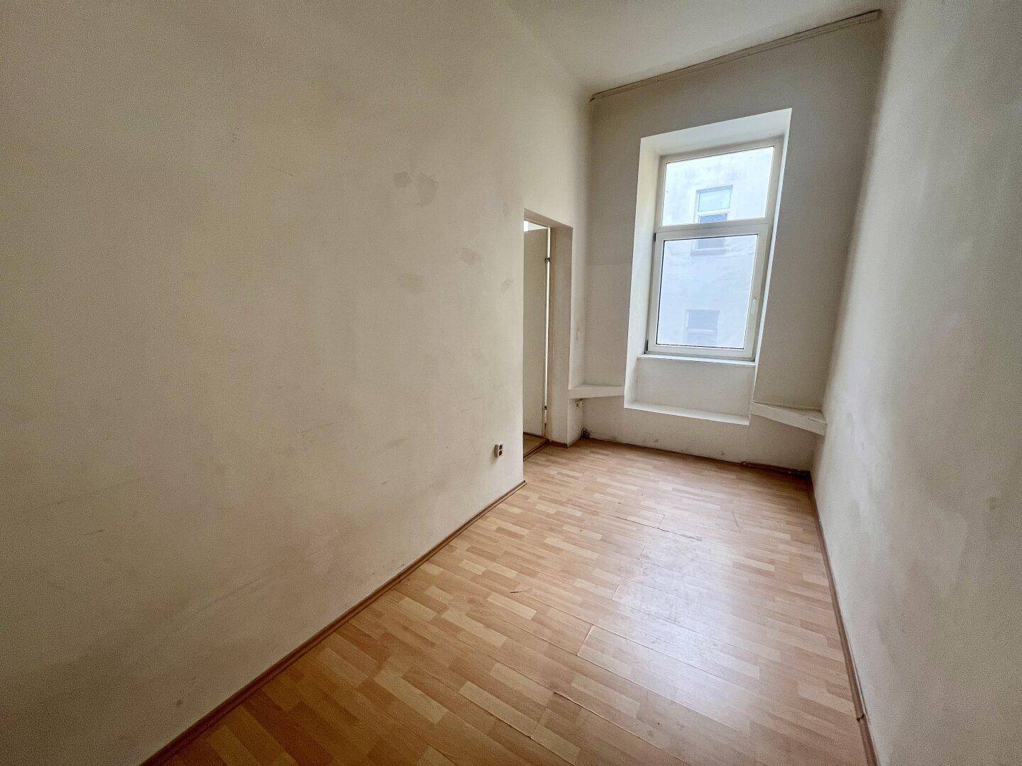 Helles Zimmer mit Laminatboden und einem Fenster, bietet Potenzial für individuelle Gestaltung.