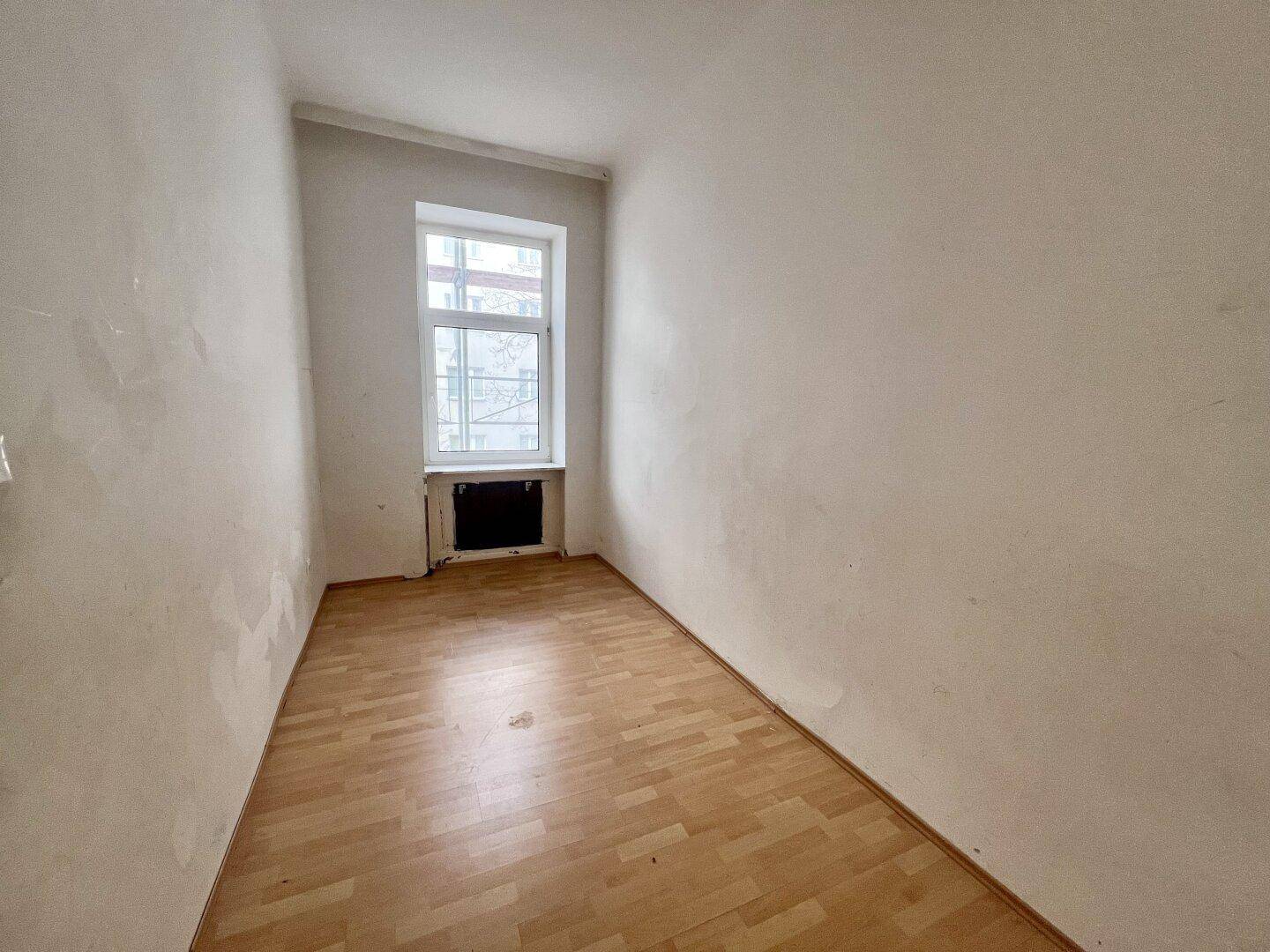Kleines Zimmer mit Laminatboden und einem Fenster, ideal als Schlafzimmer oder Arbeitsbereich.
