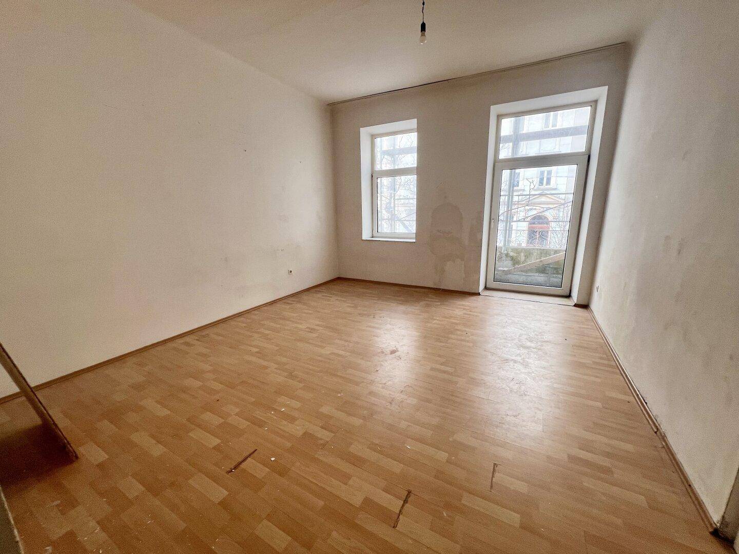 Leeres Wohnzimmer mit Laminatboden und großen Fenstern, bereit für Renovierung und Gestaltung.