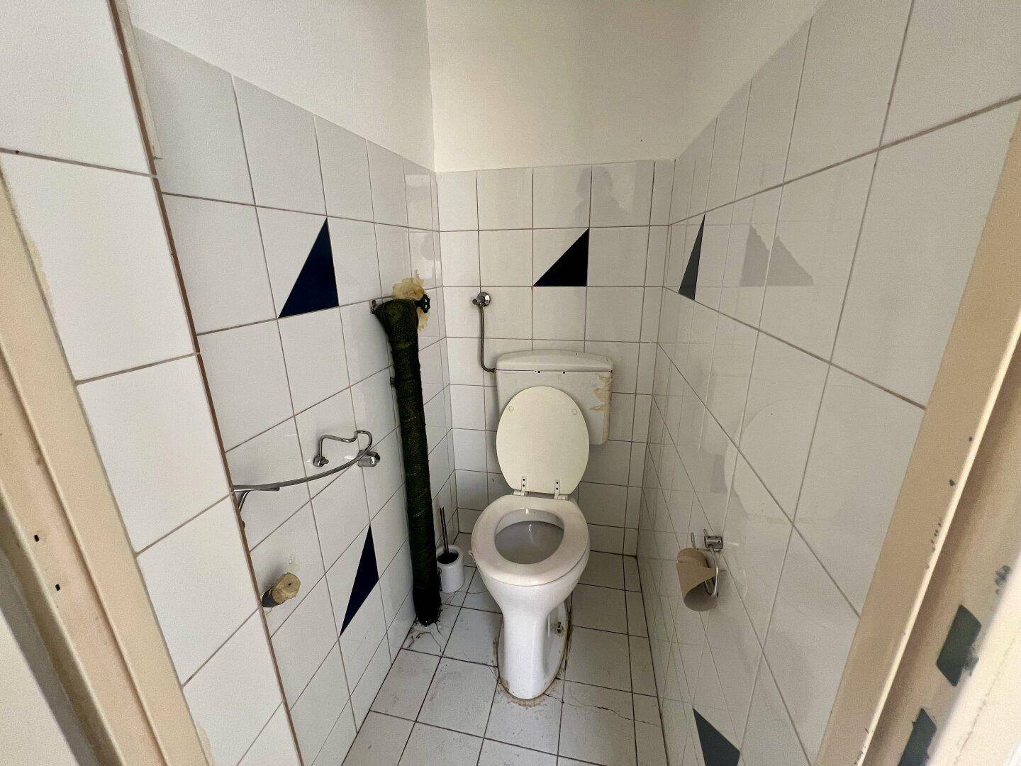 Kleines WC mit weißen Fliesen und blauen Dreiecksmustern, ausgestattet mit einer Toilette.