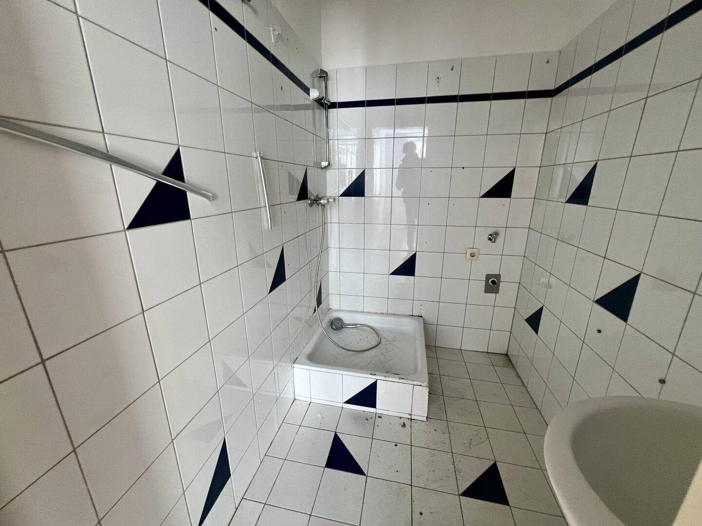 Badezimmer mit Duschbereich, weißen Fliesen und blauen Dreiecksmustern sowie einem Waschbecken.
