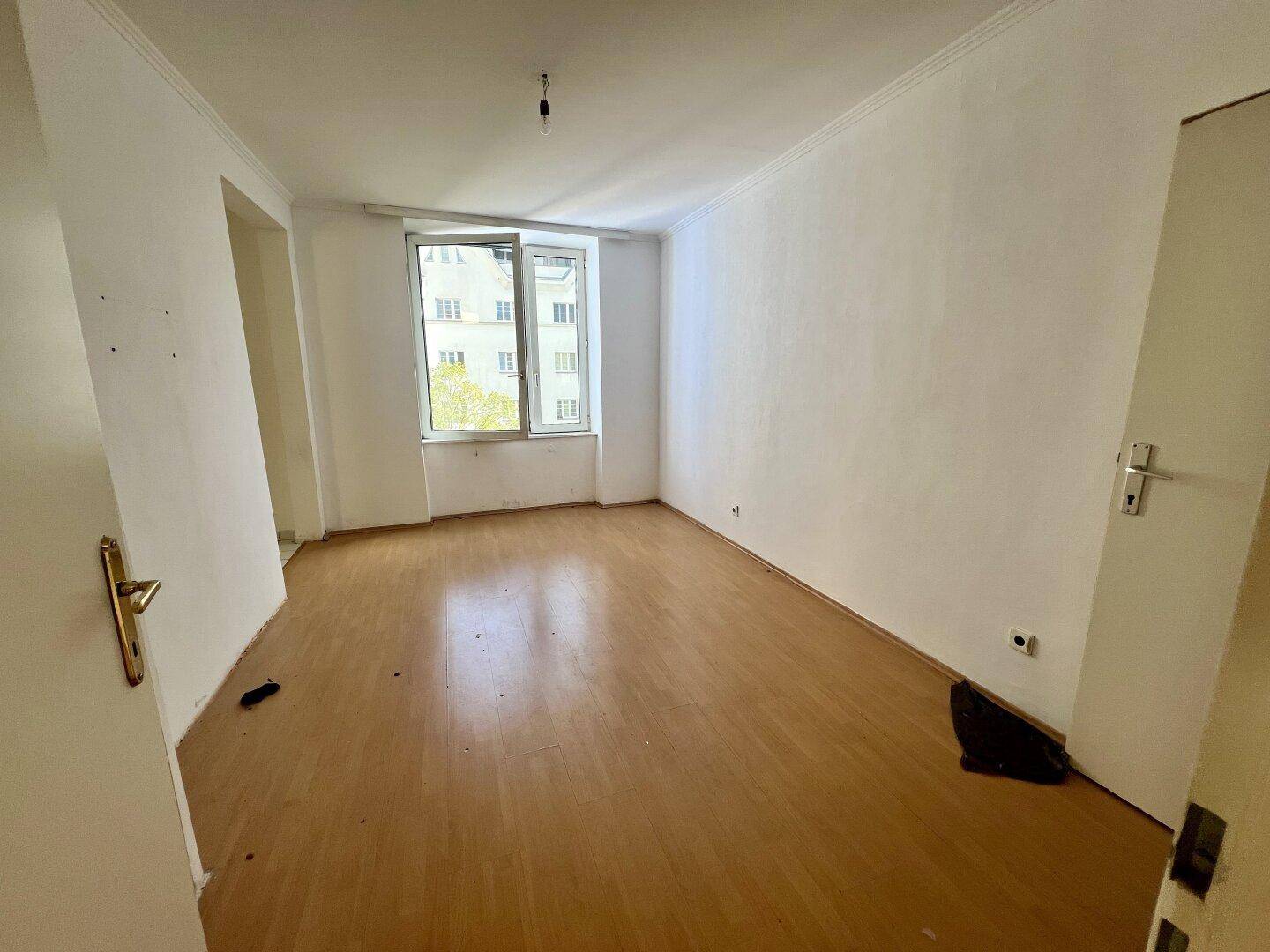 Heller, leerer Raum mit Holzparkettboden und einem großen Fenster mit Blick nach draußen.