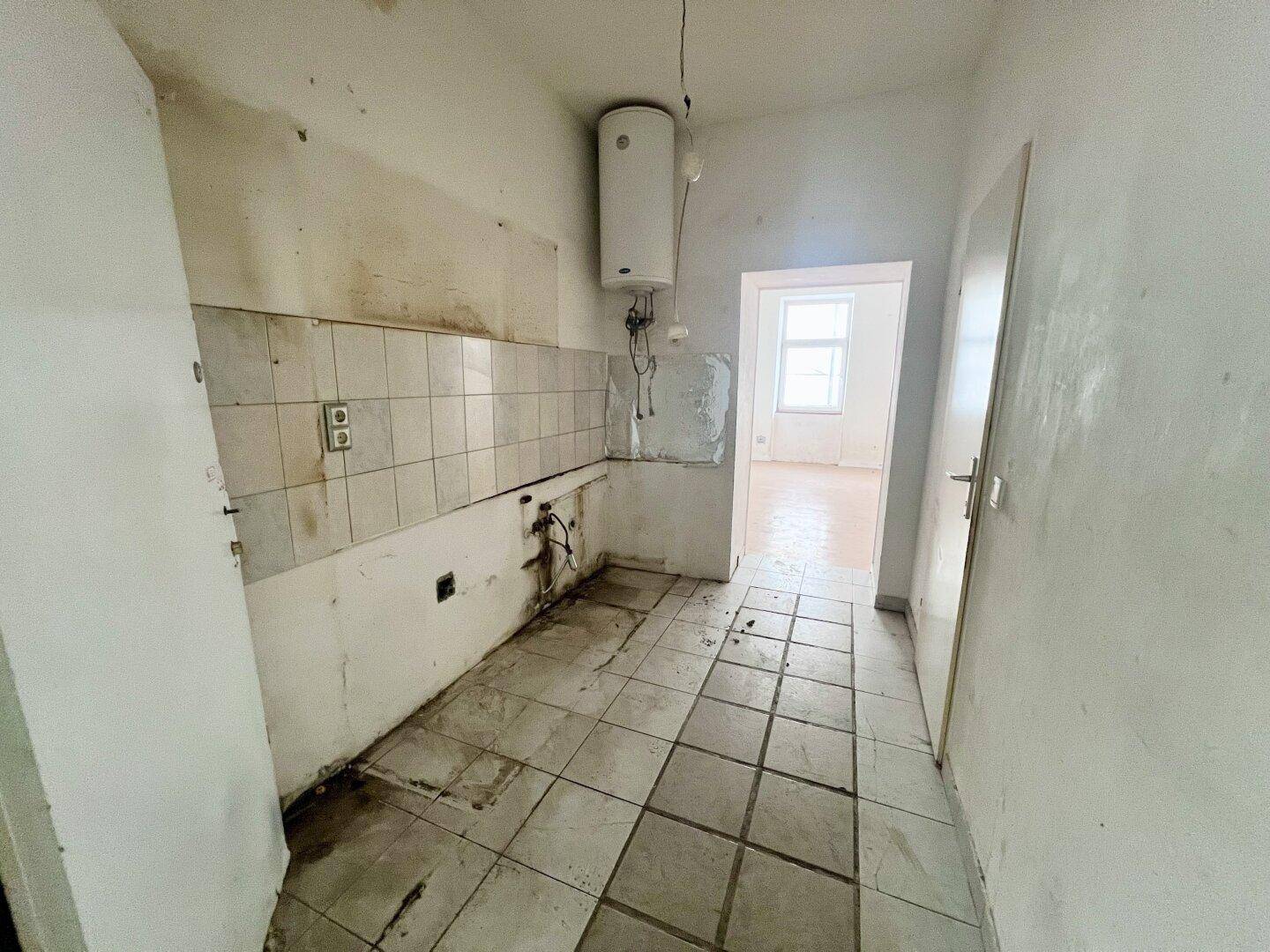 Leere Küche mit Fliesenboden, Wandfliesen und Warmwasserboiler, bereit für eine neue Einrichtung.