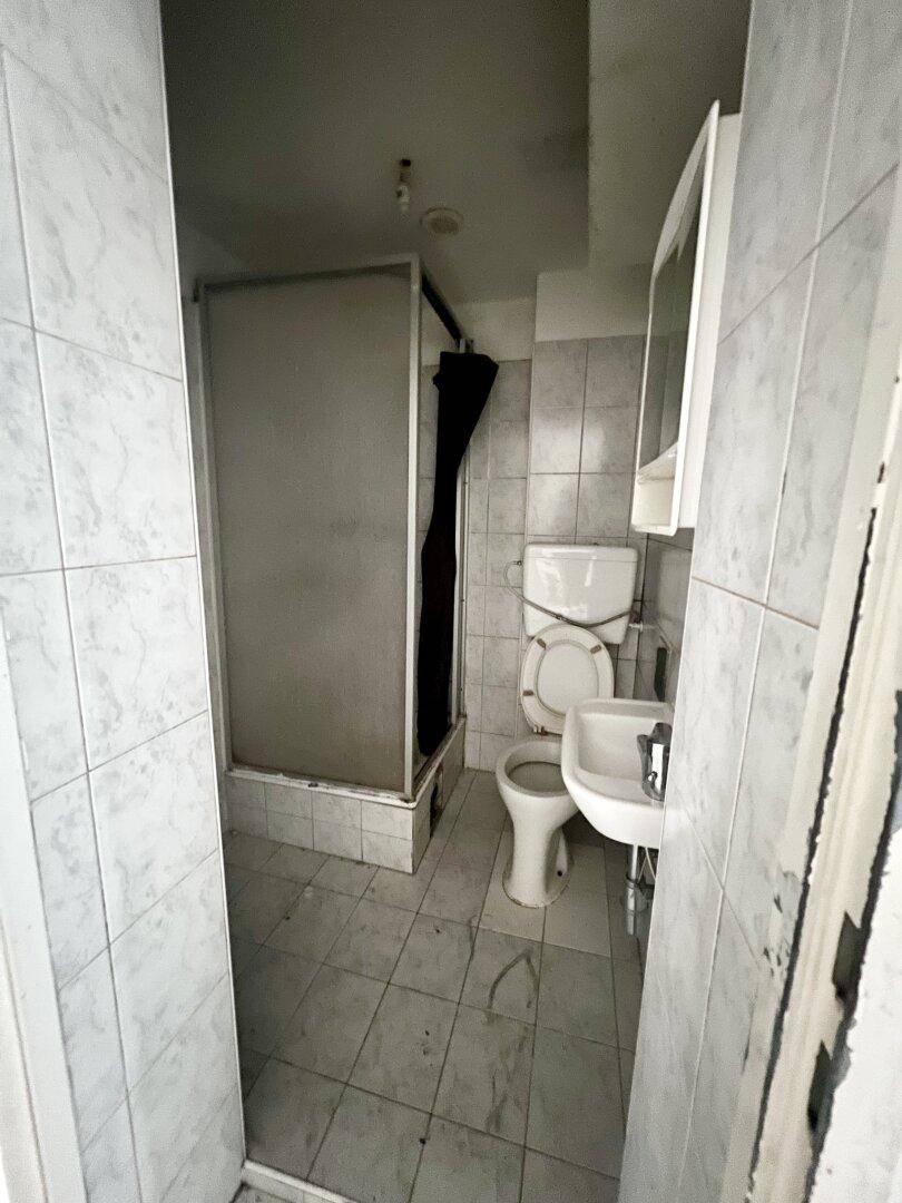 Kleines Badezimmer mit Duschkabine, WC, Waschbecken und Wandfliesen, renovierungsbedürftig.