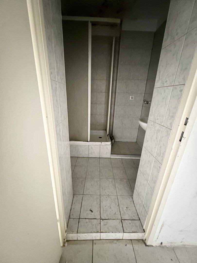 Badezimmer mit Duschkabine, Waschbecken und Fliesenboden, renovierungsbedürftig.