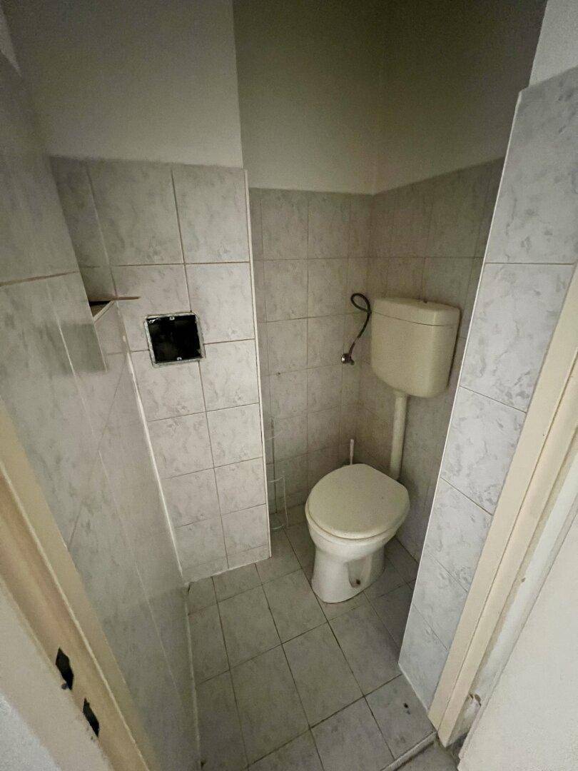 Separate Toilette mit Fliesenboden und Wandfliesen, in einfachem Zustand.