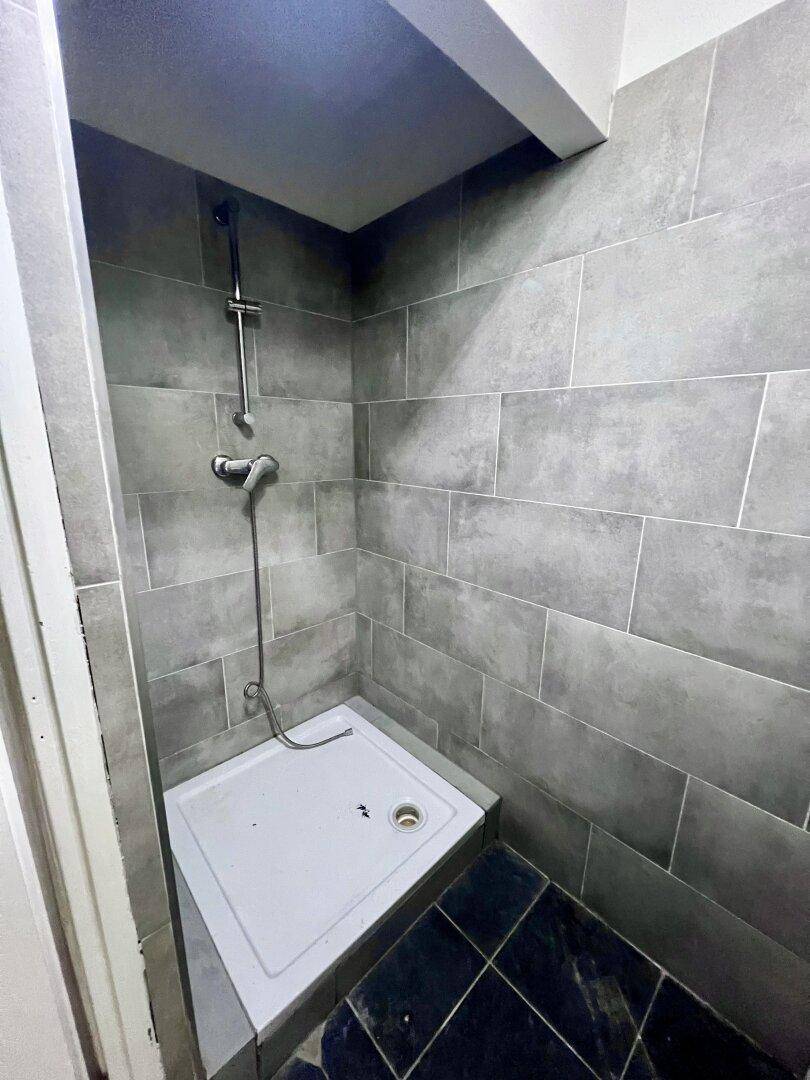 Duschbereich mit grauen Wandfliesen und einer Duschwanne in einem modernen Badezimmer.
