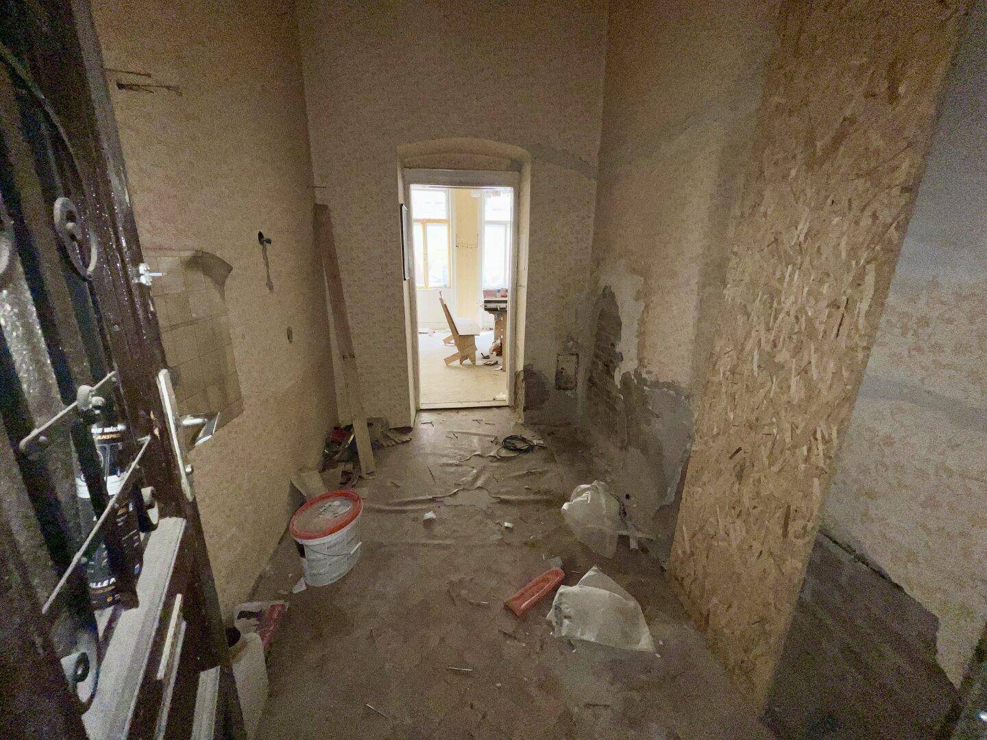 Eingangsbereich im Rohzustand mit sichtbaren Renovierungsspuren und alter Tapete.