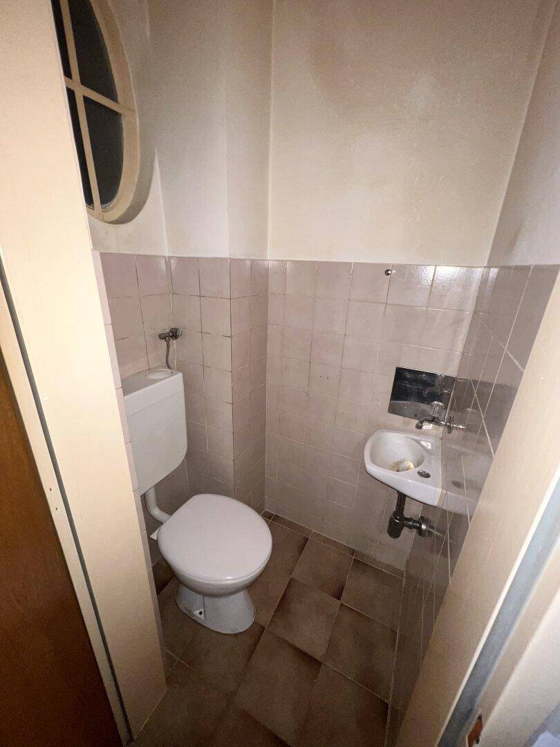 Kleines Gäste-WC mit WC, Waschbecken und einem runden Fenster.