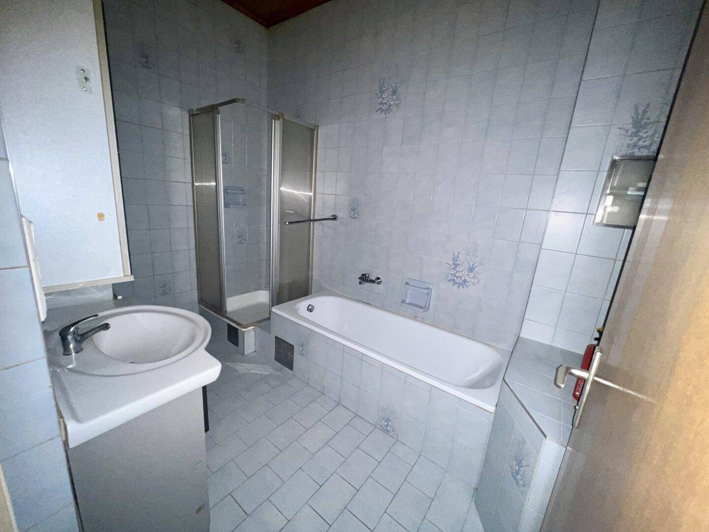 Badezimmer mit hellblauen Fliesen, Badewanne, Duschkabine und Einzelwaschbecken.