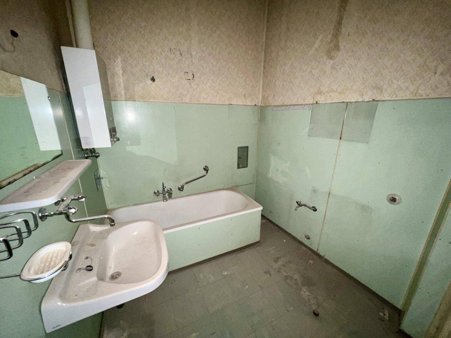Veraltetes Badezimmer mit Badewanne, Waschbecken und hellgrünen Wandpaneelen, das eine Modernisierung erfordert.