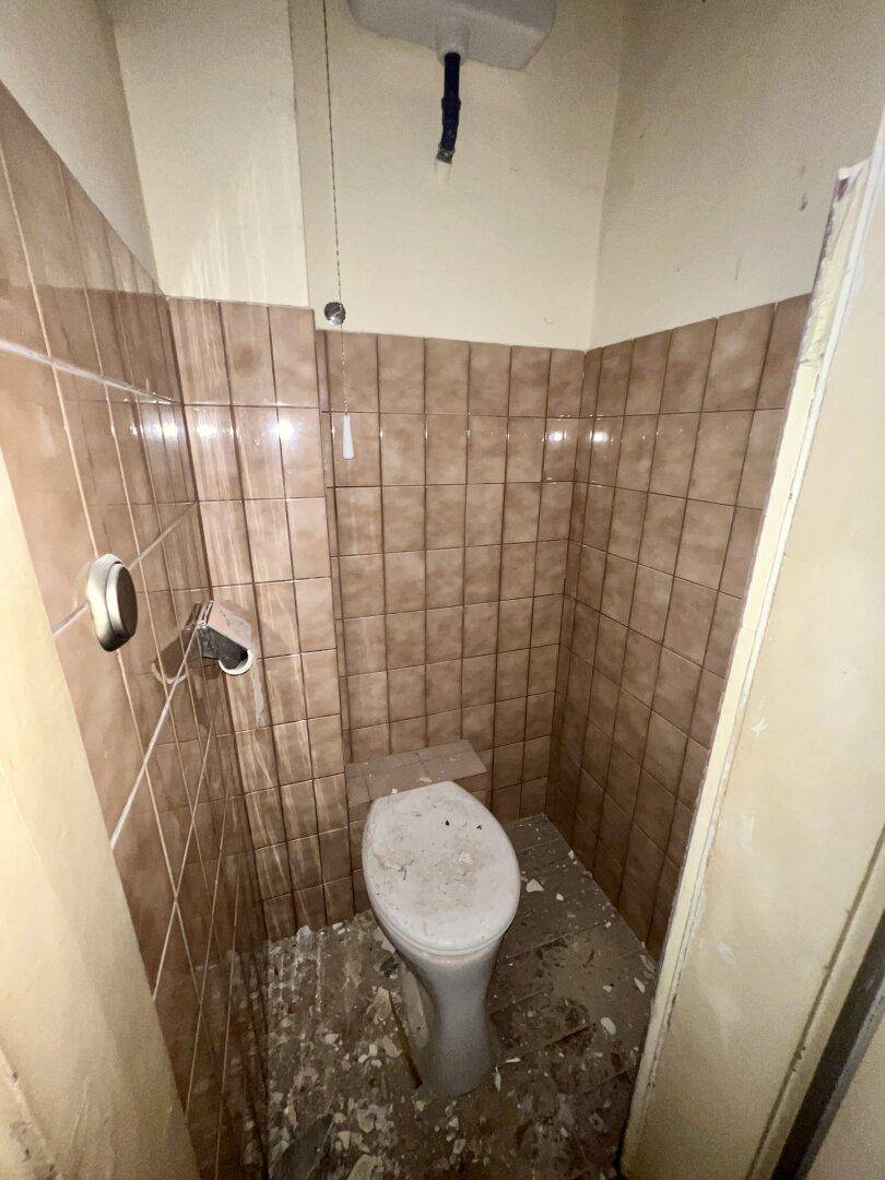 Kleiner Toilettenraum mit braunen Fliesen und WC, der dringend renoviert werden muss.