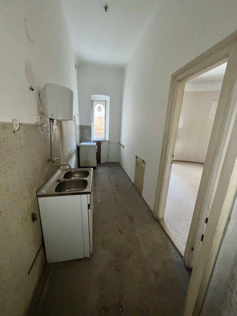 Schmaler Raum mit Spülbecken und Fenster, der eine umfassende Renovierung benötigt und als Küche dienen könnte.