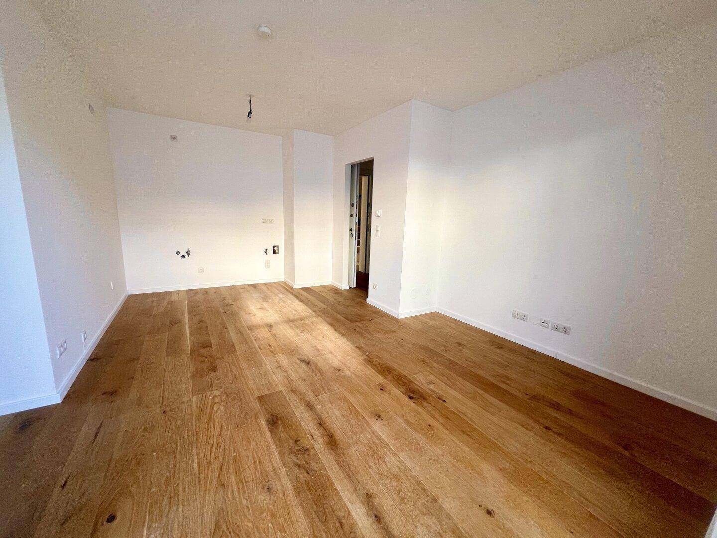 Geräumiges, leeres Zimmer mit Holzboden und weißen Wänden, bereit zur individuellen Gestaltung.