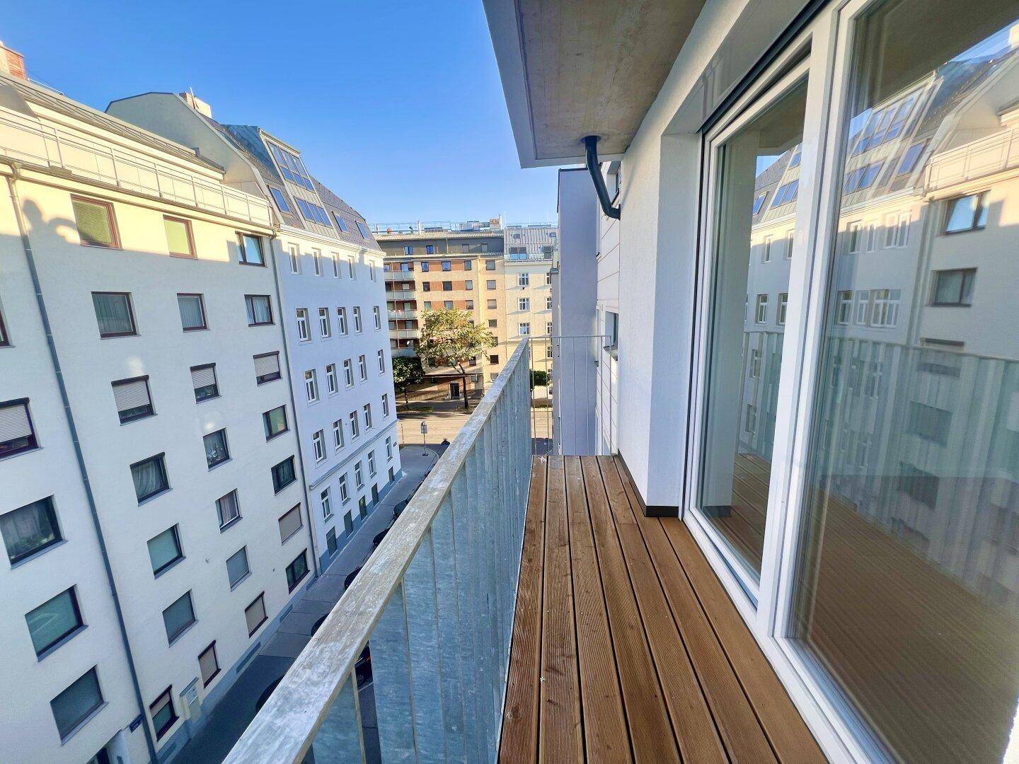 Moderner Balkon mit Holzboden und Metallgeländer, bietet einen Blick auf die Stadt.