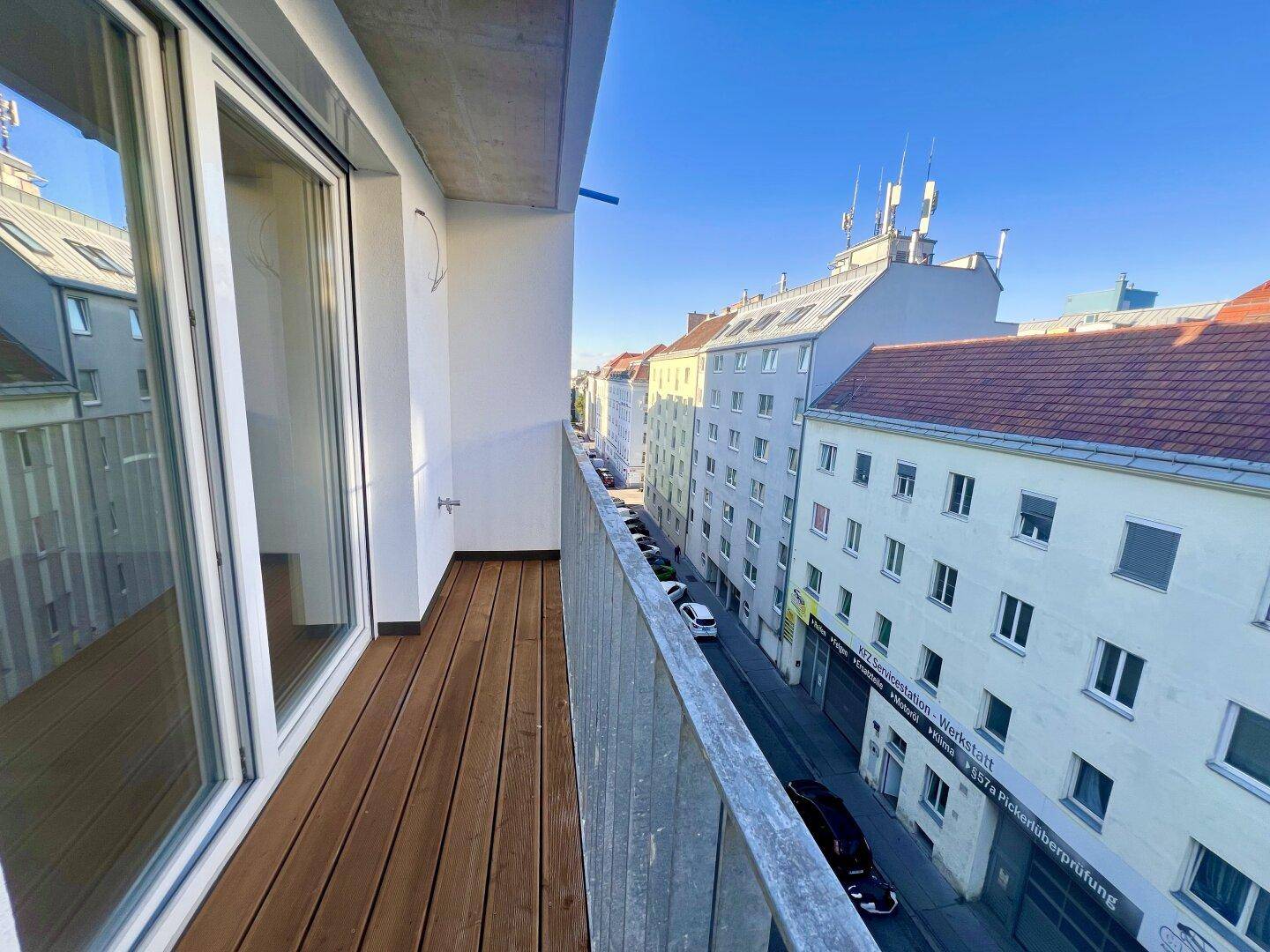 Langer Balkon mit Holzdielen und Blick auf die umliegenden Gebäude und die Straße.