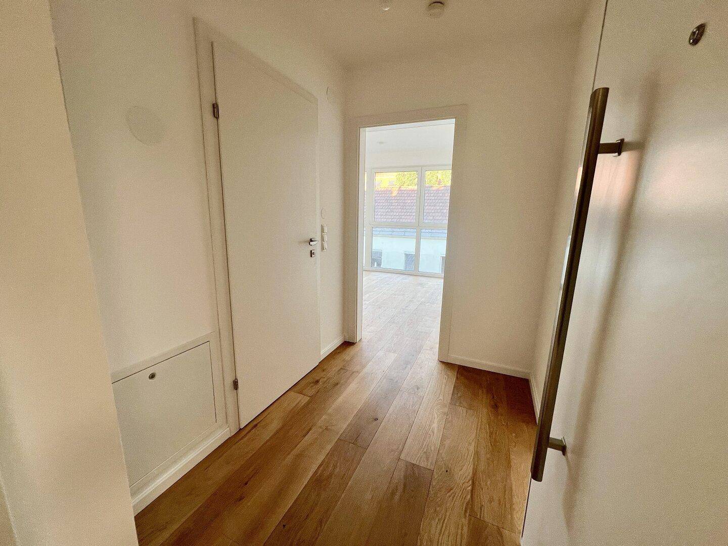 Heller Flur mit Holzboden und weißen Türen, der zu weiteren Räumen führt.