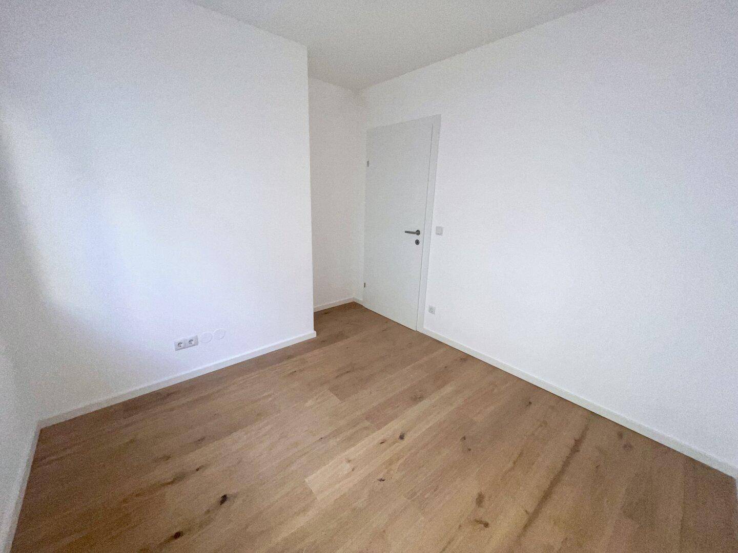 Schlichter Raum mit Holzboden und weißer Tür, bereit für die persönliche Einrichtung und Nutzung.