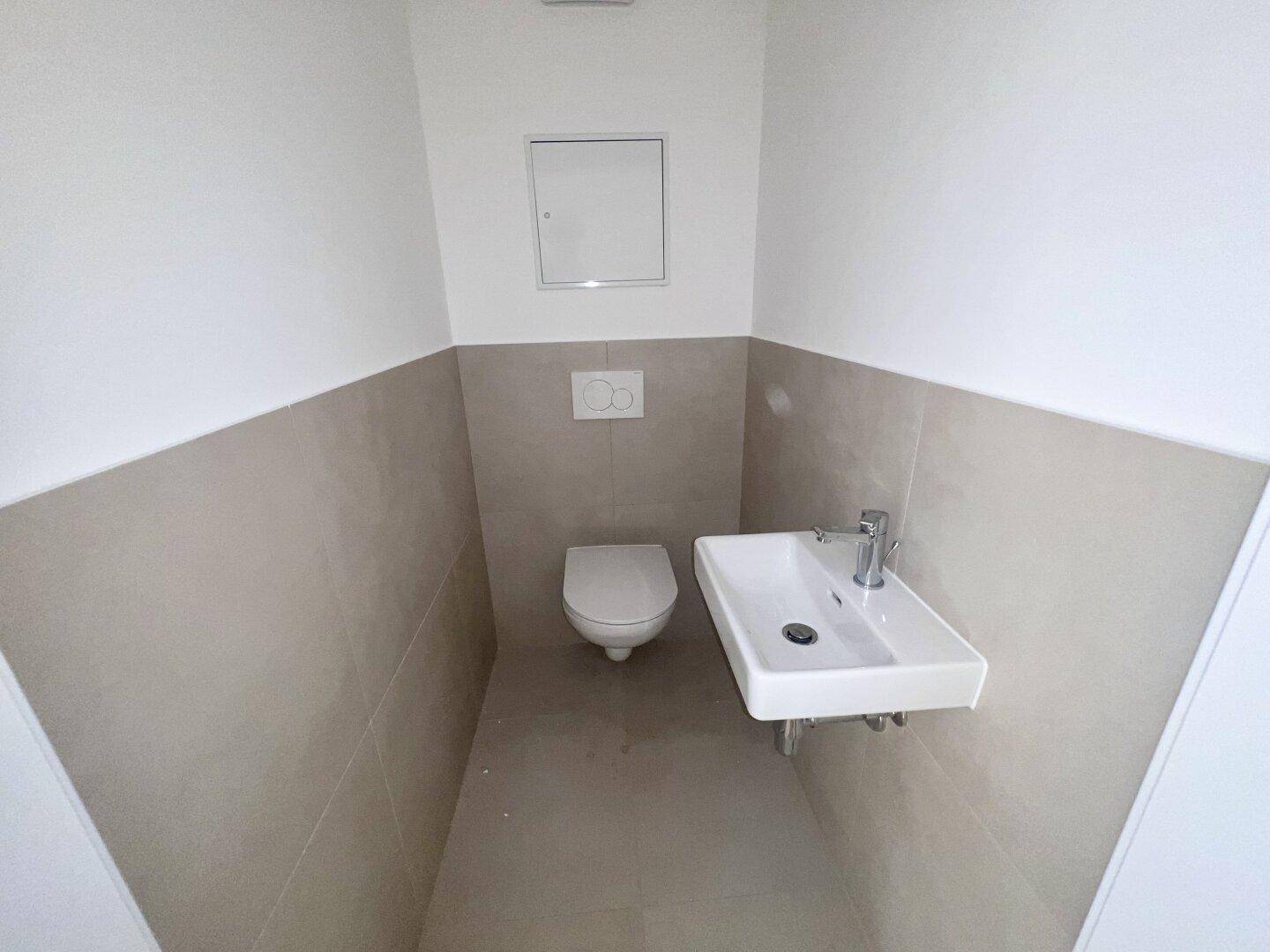 Funktionelles Gäste-WC mit wandhängender Toilette und modernem Waschbecken, halbhoch gefliest.