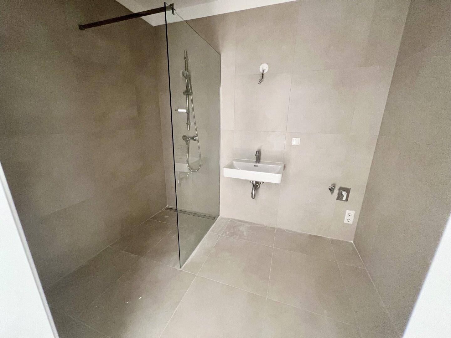 Modernes Badezimmer mit ebenerdiger Dusche, Glasabtrennung und eleganten Fliesen an Wänden und Boden.