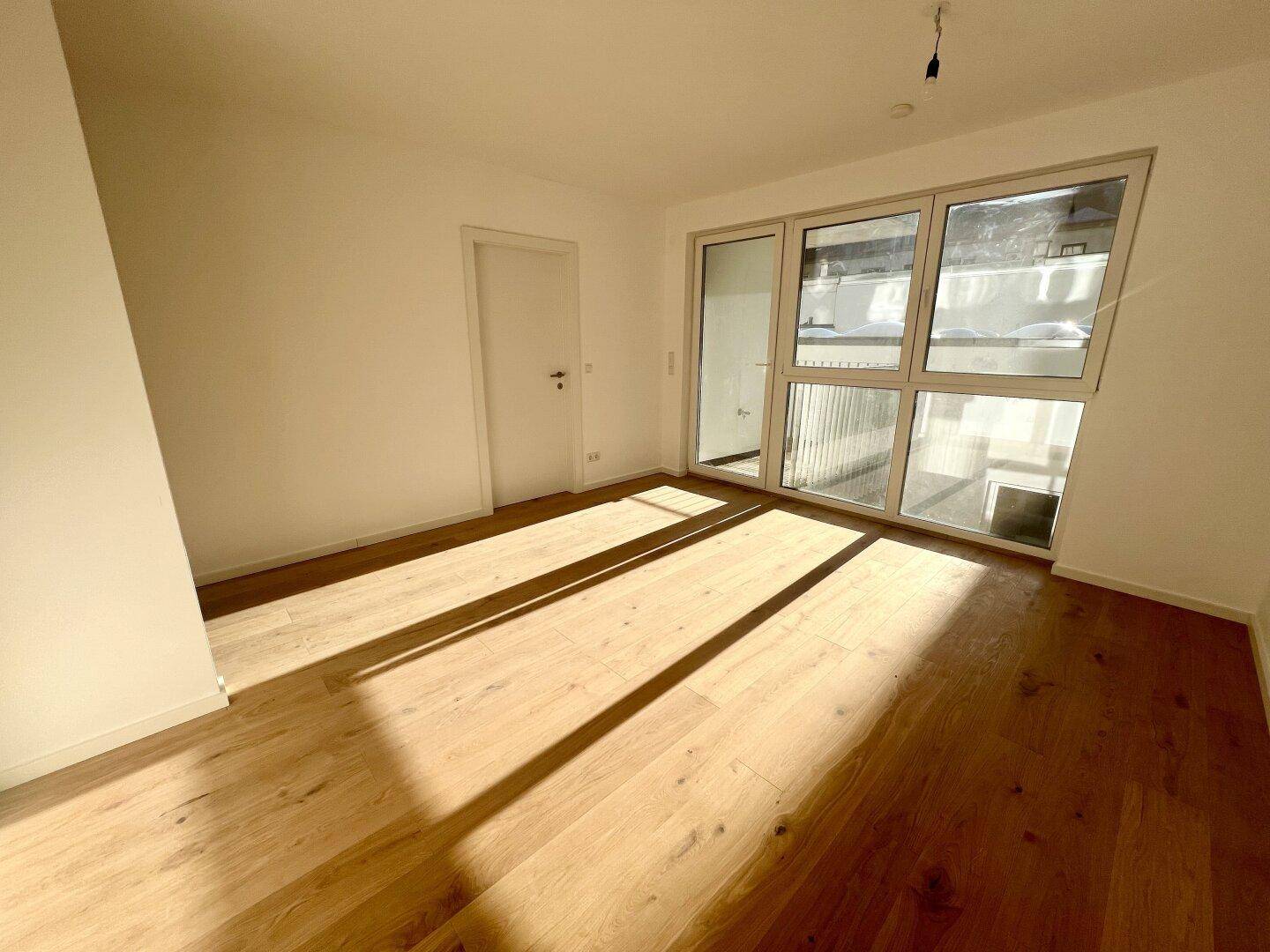 Geräumiger, heller Raum mit Holzboden und Zugang zu einem Balkon, ideal für individuelle Gestaltung.