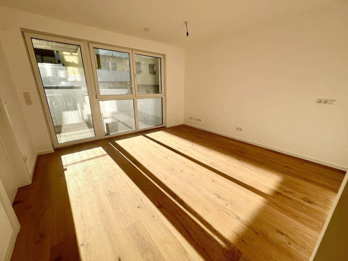 Lichtdurchfluteter Raum mit hellem Holzboden und großen Fenstern, die viel Sonnenlicht hereinlassen.
