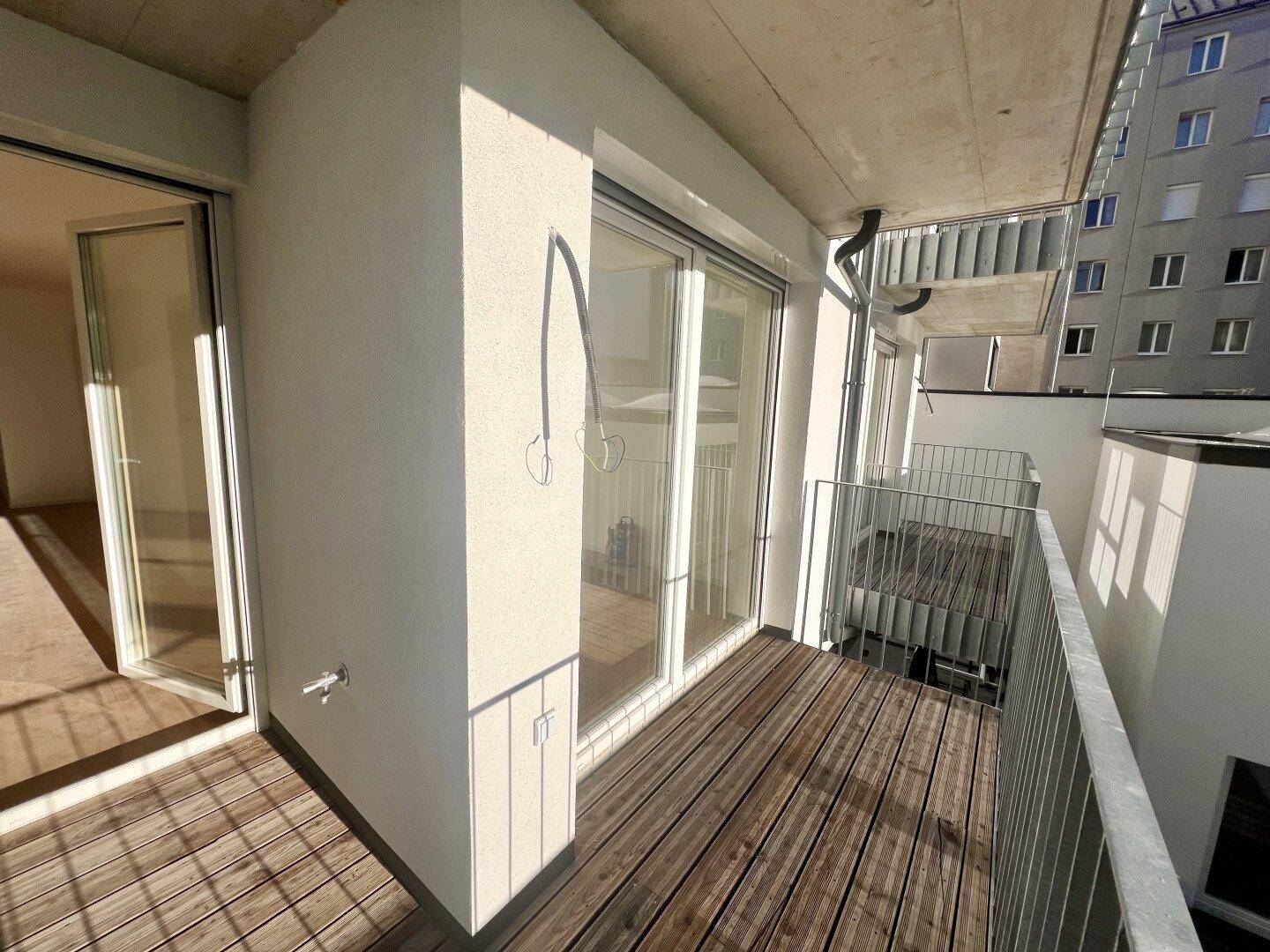 Balkon mit Holzboden und Metallgeländer, bietet einen Blick auf die umliegenden Gebäude.