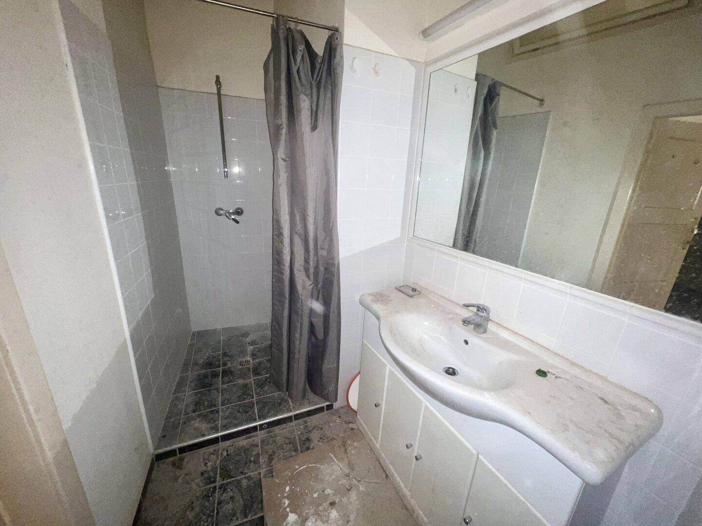 Einfaches Badezimmer mit Duschbereich und Waschbecken, renovierungsbedürftig und funktional.